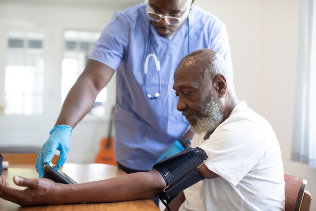 Given Pharmacy healthcare professional performing a blood pressure monitoring check-up for an elderly male patient during an in-home or community health visit.