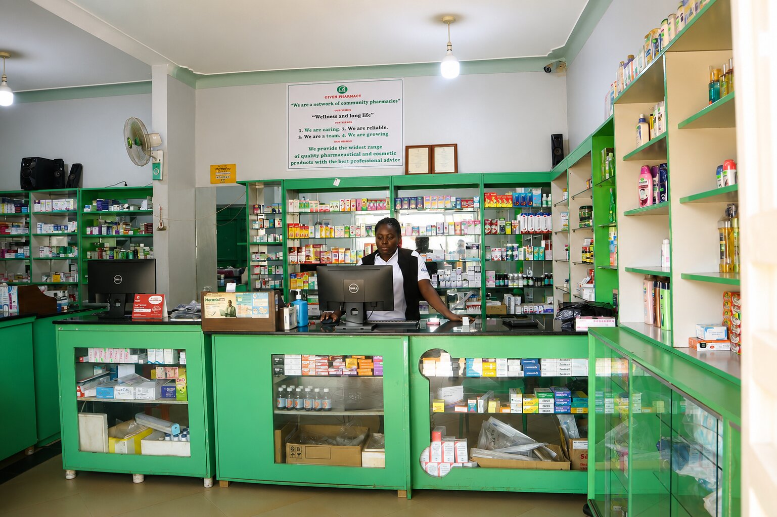 Given Pharmacy Bax Road branch interior counter with staff member serving customers opposite Jinja Main Hospital.