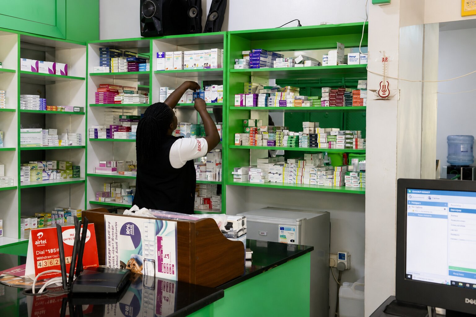 Given Pharmacy staff retrieving prescription medication from the green stock shelves.