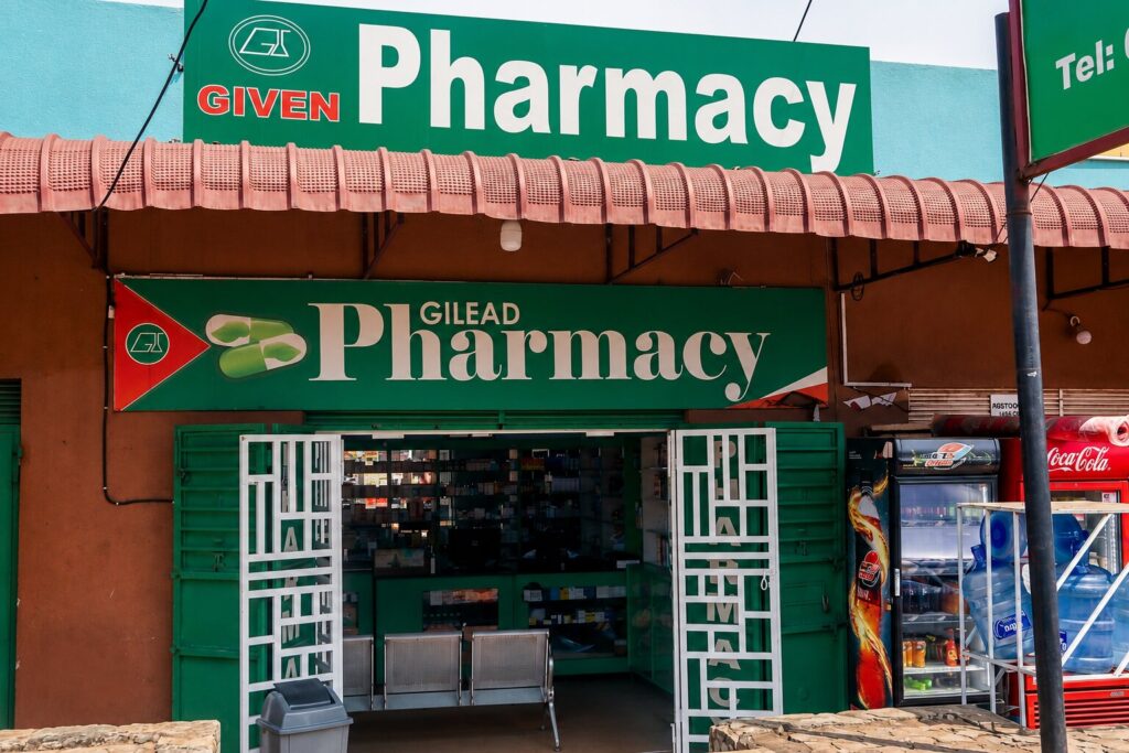 Given Pharmacy Bax Road (opposite Jinja Main Hospital) storefront with green signage, open white entrance gates, and a waiting bench.