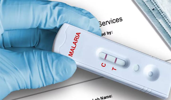 Given Pharmacy malaria rapid diagnostic test (RDT) kit displaying a positive control test result, being handled by a healthcare professional wearing protective blue nitrile gloves, representing the pharmacy's accessible on-site malaria screening and diagnostic health services.